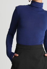 Mörkblå polotröja i ett mjukt, elastiskt tyg med långa ärmar och tumhål, i kombination med en svart högmidjad kjol.