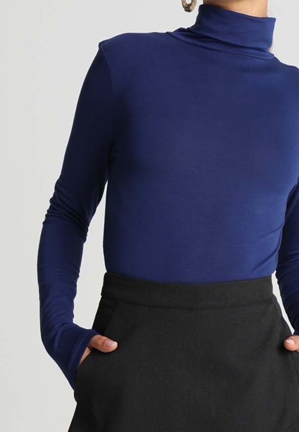 Mörkblå polotröja i ett mjukt, elastiskt tyg med långa ärmar och tumhål, i kombination med en svart högmidjad kjol.