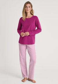 Langsleeve paars shirt gecombineerd met roest en witte gestreepte broek. Vloeiende stof, relaxte pasvorm en een eenvoudige ronde halslijn.