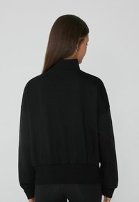 Czarny sweter z wysokim kołnierzem, długimi rękawami i ściągaczem. Wykonany z miękkiego materiału, charakteryzujący się luźnym krojem i minimalistycznym designem.