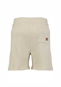 Shorts en tricot gaufré beige avec une taille élastique et une petite poche à patch sur le côté droit à l'arrière, arborant une étiquette de marque en cuir.