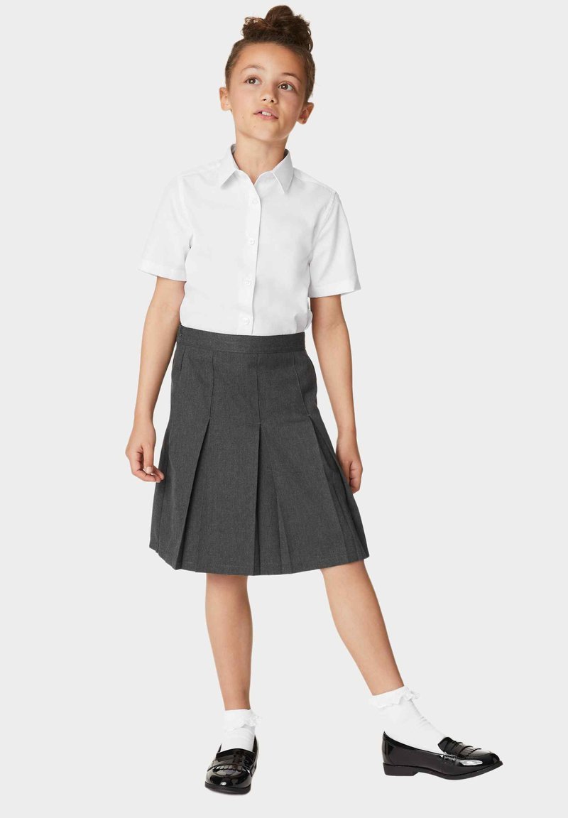Witte kortärmelige button-up shirt gecombineerd met een grijze geplooide rok. Zwarte gepatineerde leren schoenen met witte kousen met kant.