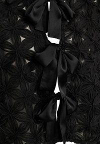 Crna čipka s cvjetnim uzorcima i satenskim mašnama sprijeda. Tekstura je delikatna i slojevita, stvarajući dubinu i kontrast.