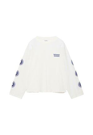 Wit shirt met lange mouwen met de tekst "between seasons" op de linkerborst en zes marineblauwe zonnestraalmotieven langs elke mouw.