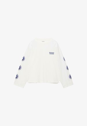 Wit shirt met lange mouwen met de tekst "between seasons" op de linkerborst en zes marineblauwe zonnestraalmotieven langs elke mouw.