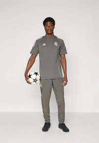 Sivi Adidas športni komplet z zgornjim delom s kratkimi rokavi z logotipom in hlačami, dopolnjen z nogometno žogo s črnimi zvezdastimi poudarki.