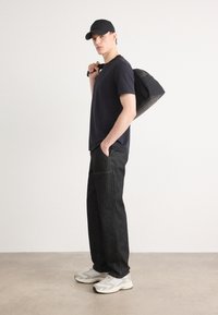 Ναυτικό μπλουζάκι, σκούρο τζιν παντελόνι με ορατά ραφές, και ανοιχτό γκρι αθλητικά παπούτσια. Μαύρο καπέλο, μαύρη τσάντα κρεμασμένη στον ώμο.