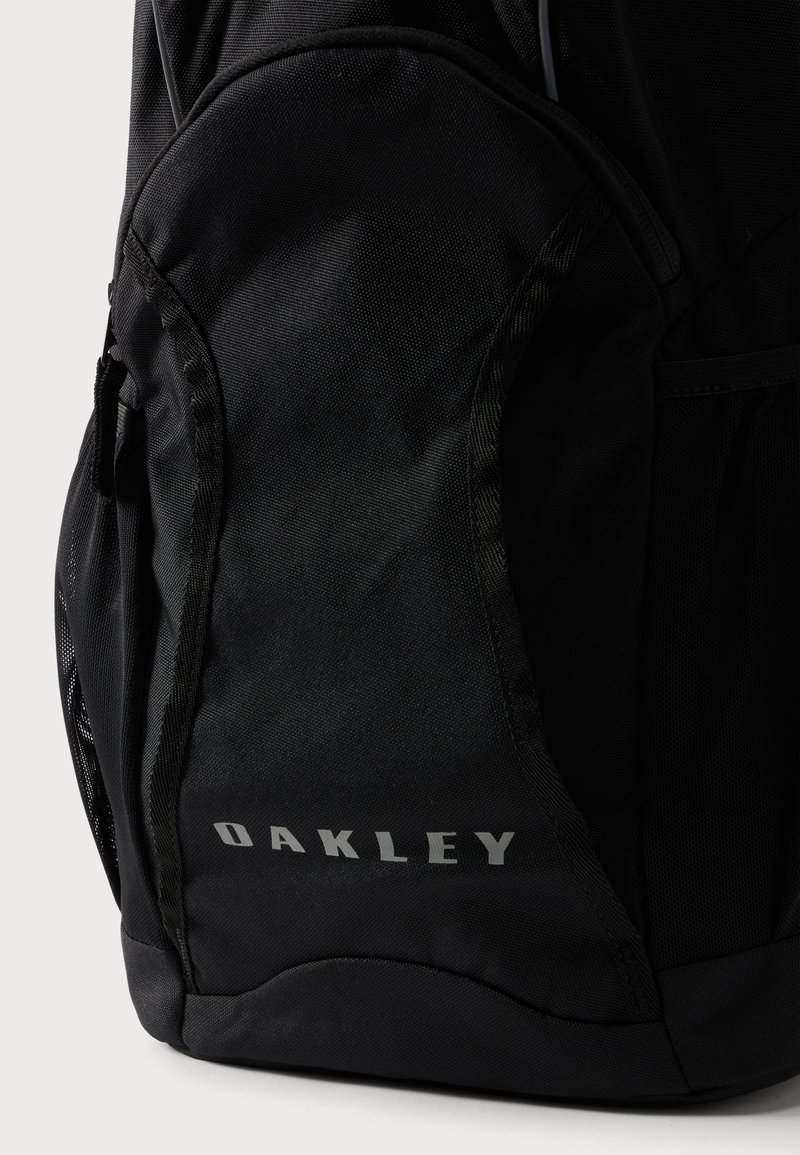 Nahaufnahme der Unterseite eines schwarzen Oakley-Rucksacks, die die Stoffstruktur und das Oakley-Logo in hellgrauen Buchstaben zeigt.