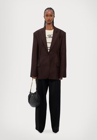 Pruun ruuduline ülicerige jakk, mustad laiad püksid, beež sviiter tumedate triipudega ja must käsitasku kuldse ahelaga.