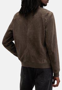 Brun ruskind jakke med en blød tekstur, ribbet kant og manchetter. Har et rent bagdesign uden yderligere udsmykninger.