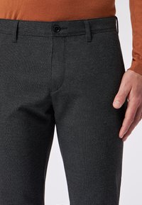 Dunkelgraue, strukturierte Hosen mit schlankem Schnitt, ausgestattet mit einem Knopfverschluss und seitlichen Taschen. Das Material wirkt gewebt und strapazierfähig.