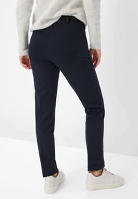 Marineblaues Slim-Fit-Hosenmodell mit glatter Textur und detailliertem Bund; kombiniert mit beigen Sneakers mit minimalistischem Design und Schnürsenkeln.