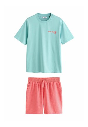 Muž nosí svetlotyrkysové tričko s červeným nápisom „Henri-Matisse“ na ľavej strane hrude na jednofarebnom béžovom pozadí.