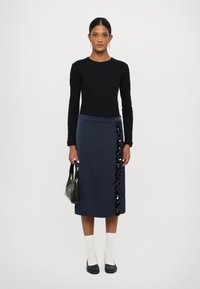 Jūras spēku midi svārki ar melnām ziedu rotām pa sāniem, kombinēti ar pieguļošu melnu garām piedurknēm topu, baltām zeķēm un melniem dzīvokļiem.