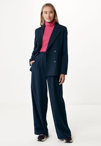 Námořnický dvouřadý blazer, top s vysokým límcem v barvě fuchsie, volné námořnické kalhoty a tmavé tenisky. Hladká látka s propracovaným střihem.