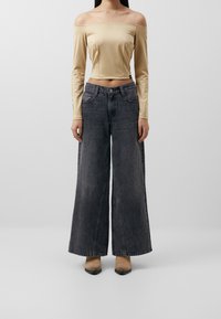 Beige off-shoulder pitkähihaine paita, joka yhdistetään korkeavyötäröisiin,  löysiin tummanharmaisiin farkkuihin. Mallilla on päällä vaaleanruskeat korolliset saappaat.