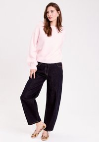 Pull en maille lâche rose clair avec un col rond et des manches longues, associé à un pantalon ample en denim foncé et des chaussures plates à imprimé floral.