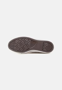 Sola de sapato de borracha castanha com padrão de aderência texturizado, com um acabamento branco nas laterais e uma forma ligeiramente curvada; apresenta a marca "Converse All Star."