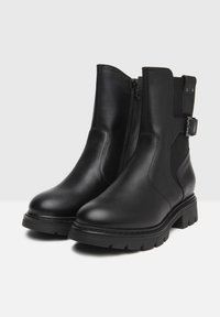 Black leather ankle boots featuring a side zipper, elastic panels, and a decorative buckle on the outer side. Textured rubber sole.