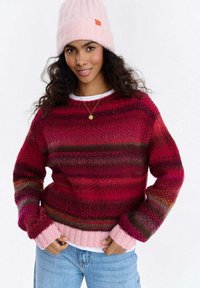 Sweter na drutach z poziomymi czerwono-różowymi paskami, z prążkowanymi mankietami i dołem; w zestawie z jasnoróżową dzierganą czapką.