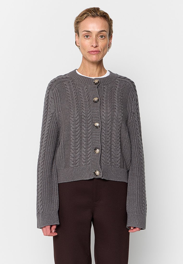 Gilet en tricot gris avec un col rond, motifs texturés et gros boutons sur le devant, longueur raccourcie et manches surdimensionnées.