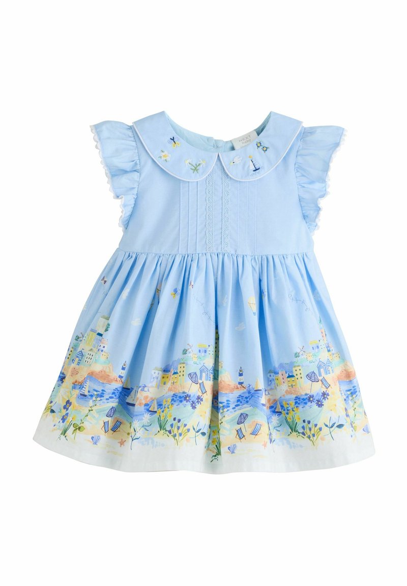 Robe en coton bleu avec des manches volantes, un col rond et une scène côtière colorée brodée au bas. Le motif comprend des fleurs et des bâtiments.