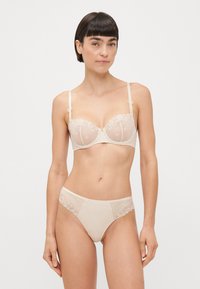 Soutien-gorge en dentelle beige et culotte assortie avec un tissu transparent, une broderie florale et des bretelles ajustables. Comprend des accents décoratifs sur les bretelles.