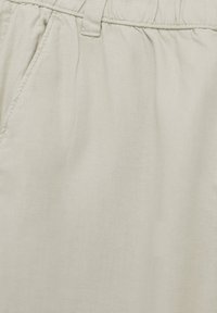 Close-up of light beige pants with elastic waistband, belt loop, and side pocket stitching detail.