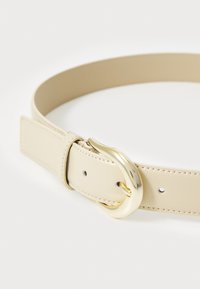 Beige lærbelte med en blank gullspenne. Har flere huller for justering og en glatt tekstur. Enkelt design, litt avrundet form.