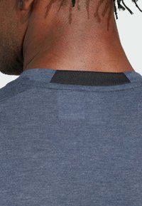 Camisa azul de manga corta con un tejido texturizado, escote redondeado y un contraste negro en la parte posterior del cuello.