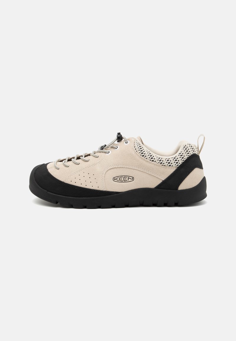 Beige suede shoe with black rubber toe cap and sole, featuring a lace-up design and breathable mesh accents on the heel.