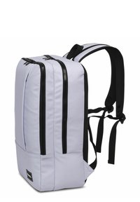 Mochila de color púrpura claro con dos cremalleras negras, correas acolchadas negras, forma rectangular y textura de tela suave. Presenta un logo en la parte frontal.