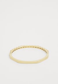 Bague en métal doré de forme octogonale, avec un bord texturé et des détails perforés à l'intérieur.