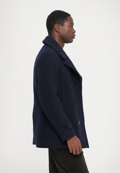 Casaco peacoat de lã azul-marinho com um colarinho largo, botões duplos e bolsos laterais. A textura é suave, com um corte ajustado.