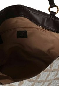 Grote tote bag met een textuur aan de buitenkant en een geometrisch patroon in lichtbeige en roomkleur, bruin leren afwerking en een ritssluiting in het binnenvak.