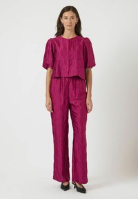 Fuksia kaksiosainen asu, joka sisältää lyhyen paidan puffiholveilla ja teksturoidulla aallokkomallilla, yhdistettynä suoriin housuihin.