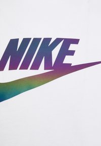 Vit T-shirt med en stor, gradient "NIKE"-logotyp i lila och grön med en kurvad swoosh-design nedanför i matchande färger.