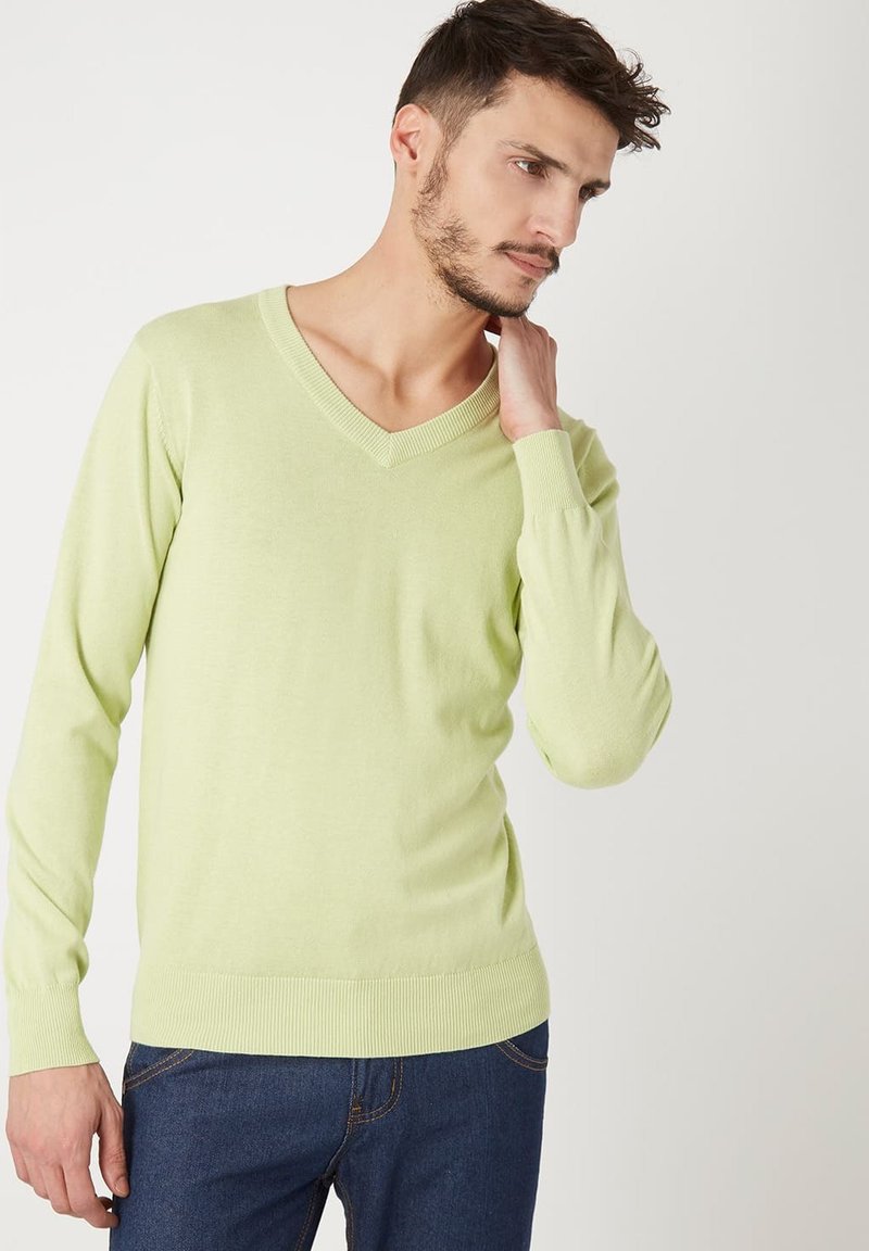 Suéter verde claro con cuello en V, mangas largas y puños acanalados. La tela parece suave y lisa, combinado con jeans azules.