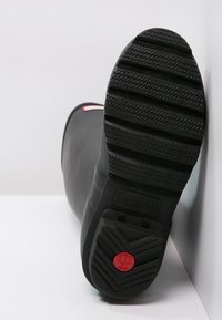 Botas de lluvia de goma negra con suela texturizada, que presentan un destacado logo rojo, un acabado suave y un diseño de punta redondeada.