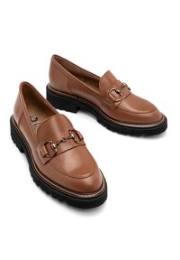 Brązowe skórzane loafersy z szerokim paskiem i metalowym detalem, płaską czarną gumową podeszwą oraz okrągłym noskiem. Minimalne akcenty w postaci szwów.
