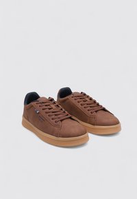 Zapatillas deportivas de cuero marrón con suelas de goma, que presentan una punta redondeada, diseño con cordones y sutiles acentos de la marca en azul. Textura suave.