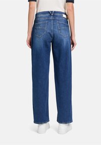 Blauwe denim wijde broek met een hoge taille, twee achterzakken en een nette afwerking aan de zoom. Gecombineerd met witte sneakers.