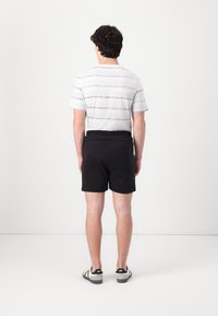 Black shorts with an elastic waistband, paired with a striped shirt in light gray and dark gray tones, worn with casual shoes.