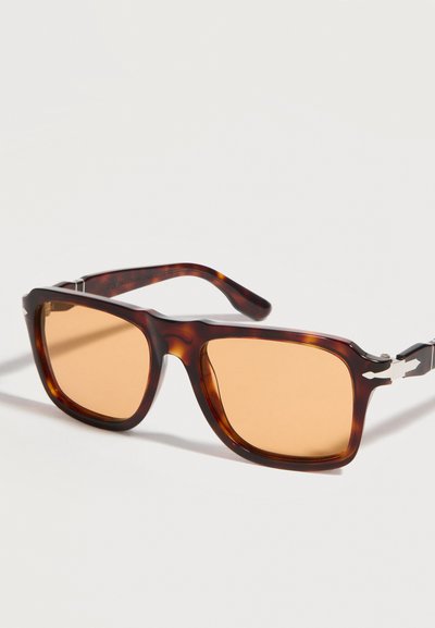 Ορθογώνια γυαλιά ηλίου με καφέ-πορτοκαλί αποχρώσεις και πορτοκαλί φακούς, με ασημένιες λεπτομέρειες στις μεντεσέδες, παρουσιάζονται πάνω σε λευκό φόντο.