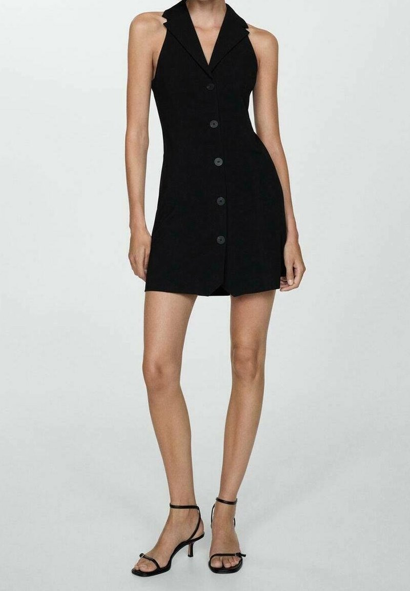 Femme mince portant une mini-robe noire sans manches boutonnée avec col et des sandales noires à talons avec brides, sur un fond uni.