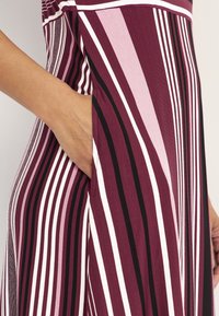 Gestreiftes Kleid mit vertikalen Linien in den Farben Burgunderrot, Pink und Schwarz. Verfügt über eine seitliche Tasche für zusätzlichen Komfort.