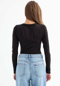 Top negro de manga larga con escote redondo, combinado con unos vaqueros de tiro alto en un tono azul claro que cuentan con bolsillos traseros y un corte relajado.