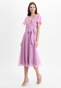 Hellblaues Kleid mit kurzen, flatternden Ärmeln, V-Ausschnitt, tailliertem Bund und fließendem Rock; getragen mit silbernen Strappy-High-Heels.