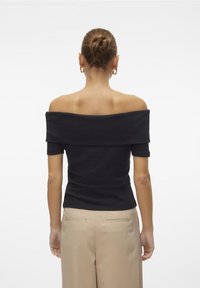 Svart av-shoulder topp med korte ermer, tettsittende design, ribbestrikket tekstur og vid halsutskjæring. Kombinert med lyse beige bukser.