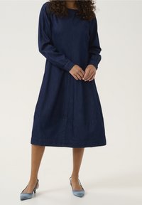 Marinblå denimklänning med långa ärmar, rundhalsad och elastiska manschetter. Skärningslängd nedanför knäet med plisserad kjol och sidofickor.